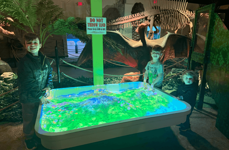 Visitors engaging with an interactive adventure exhibit at Jurrasic Gardens at Volo museum, using hands-on displays and activities