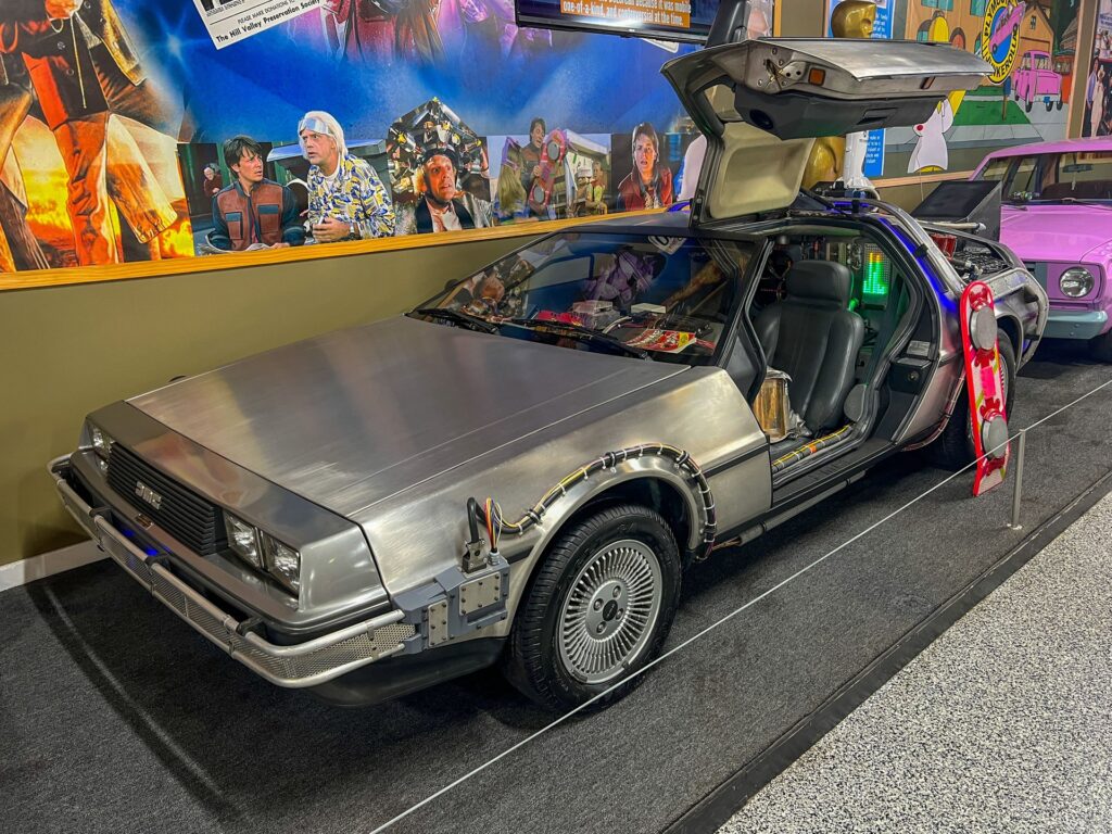 Front-three-quarter view of a 1981 DeLorean DMC-12 sports car with brushed stainless-steel body panels and distinctive upward-hinging gull-wing doors, iconic for its sleek 1980s design and pop-culture status.