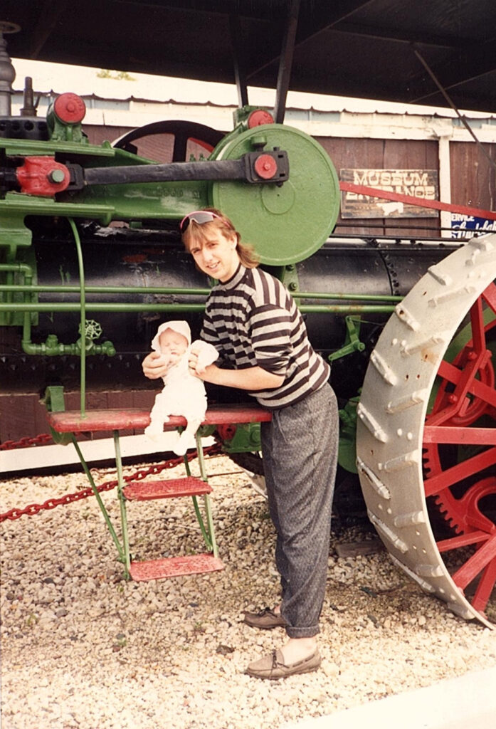 Woman holding baby near tractor.