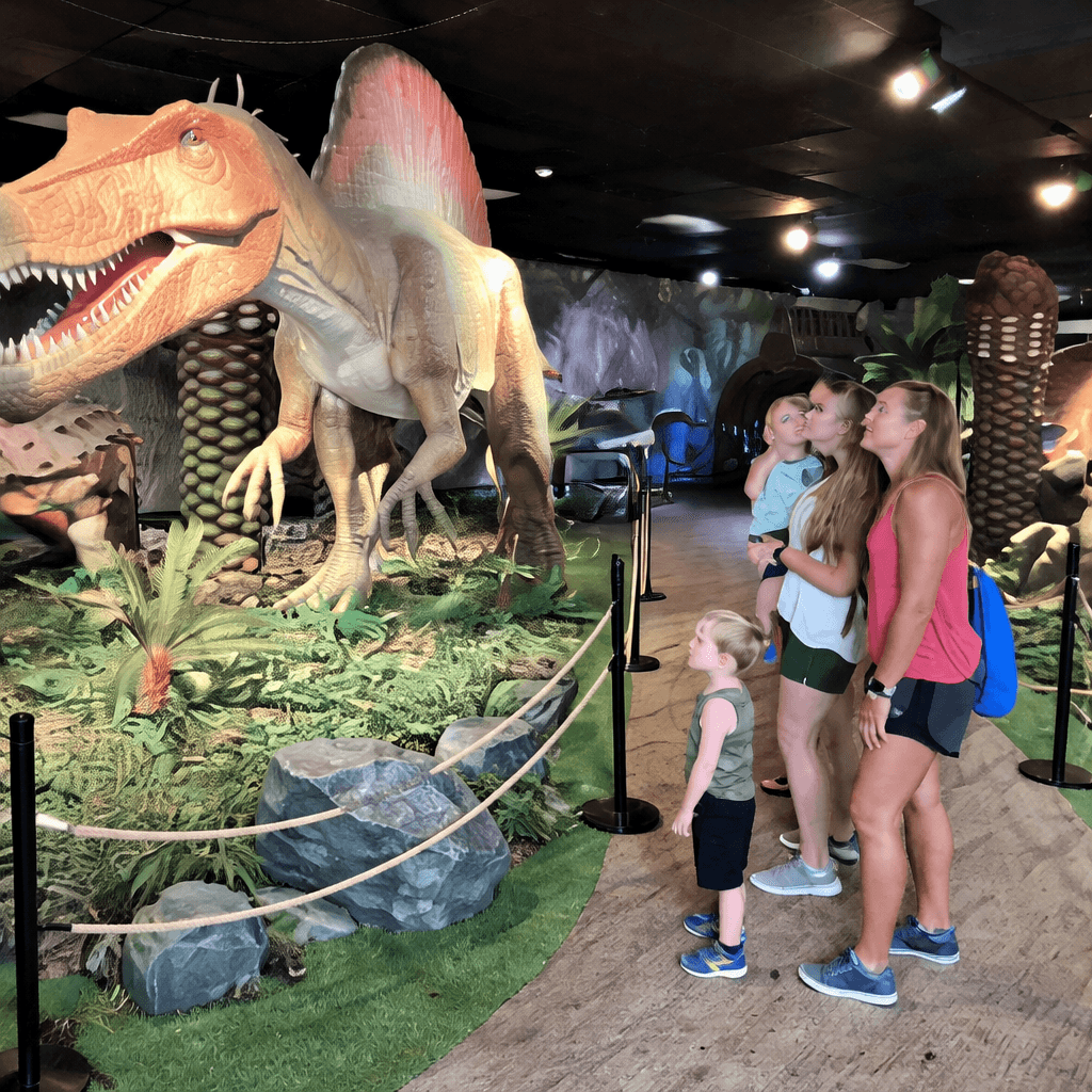 Family observing dinosaur exhibit indoors.