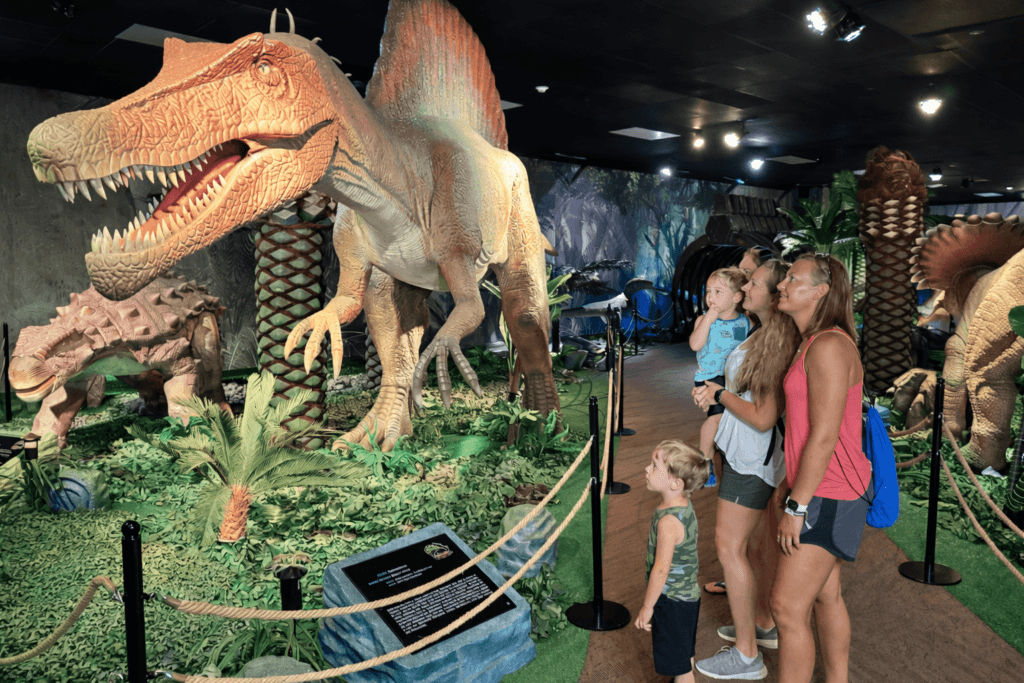 Family observing dinosaur exhibit indoors.