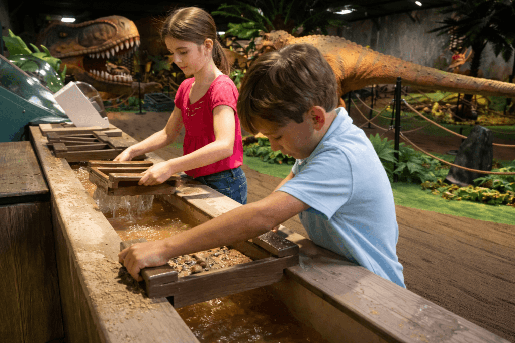 Children mining for gold in a dinosaur exhibit.