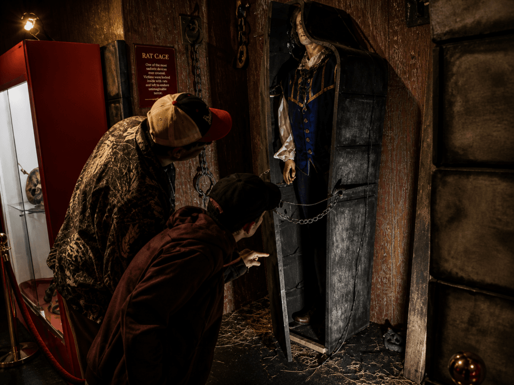 Two people examining a torture device inside of the crime and punishment display